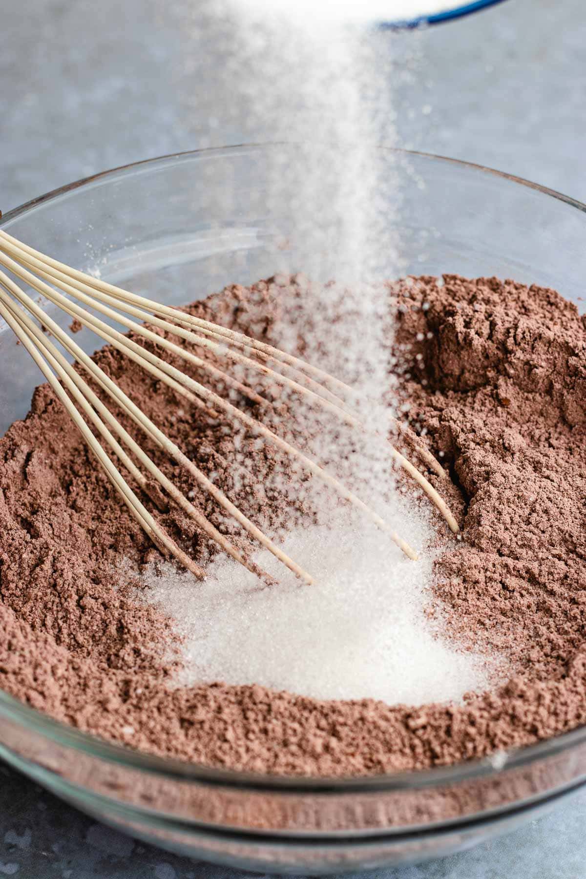 adding sugar to chocolate flour in bowl with whisk