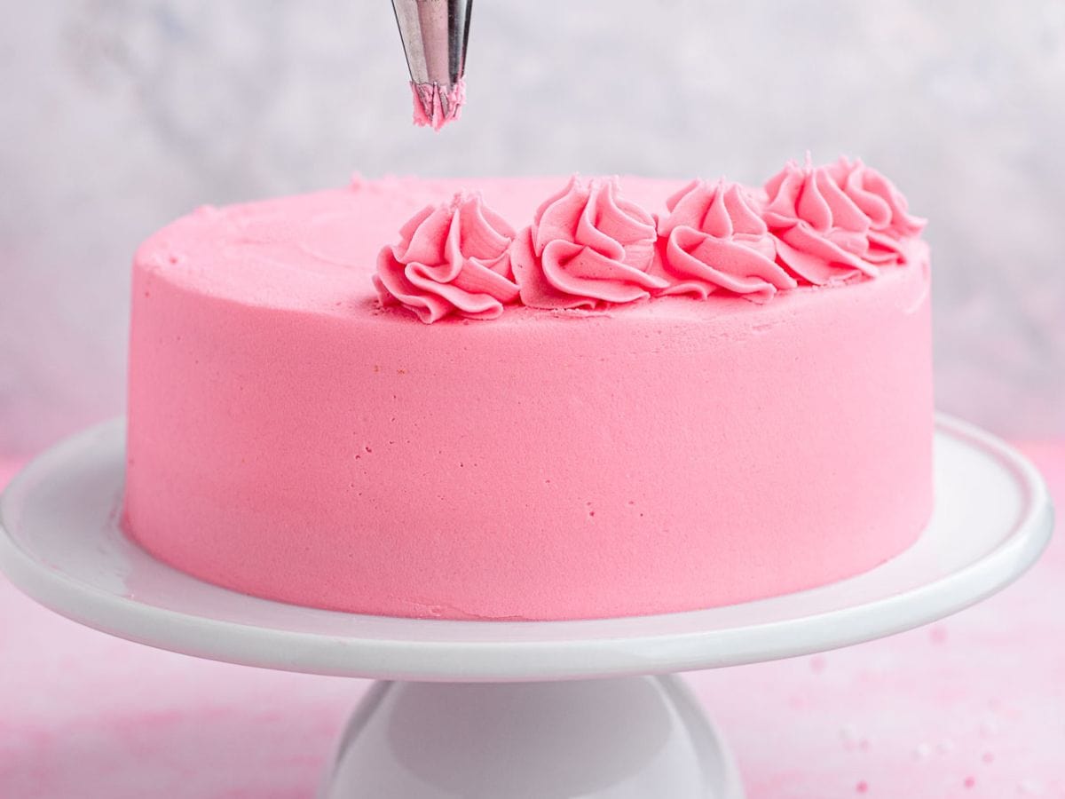Piping pink frosting over cake