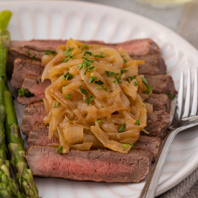 caramelized onions on steak next to asparagus on a plate