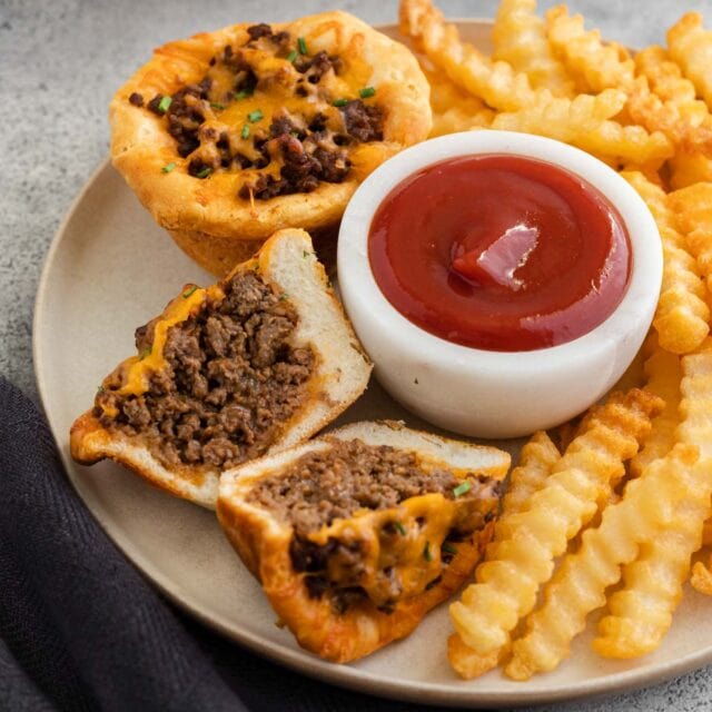 1 whole, one halved Cheesy BBQ Beef Bites on a plate with ramekin of ketchup and fries