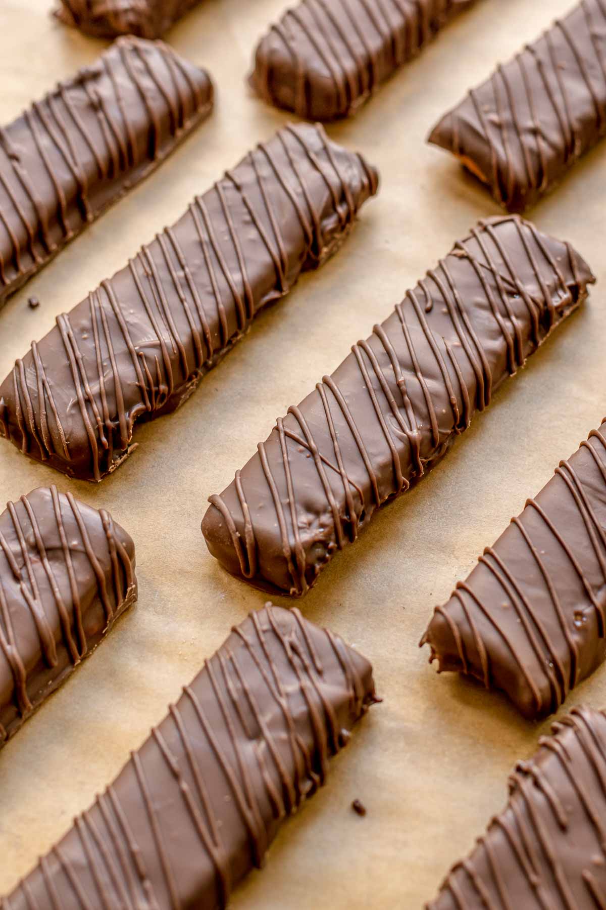 Butterfinger Bars lined up on parchment paper after adding chocolate drizzle