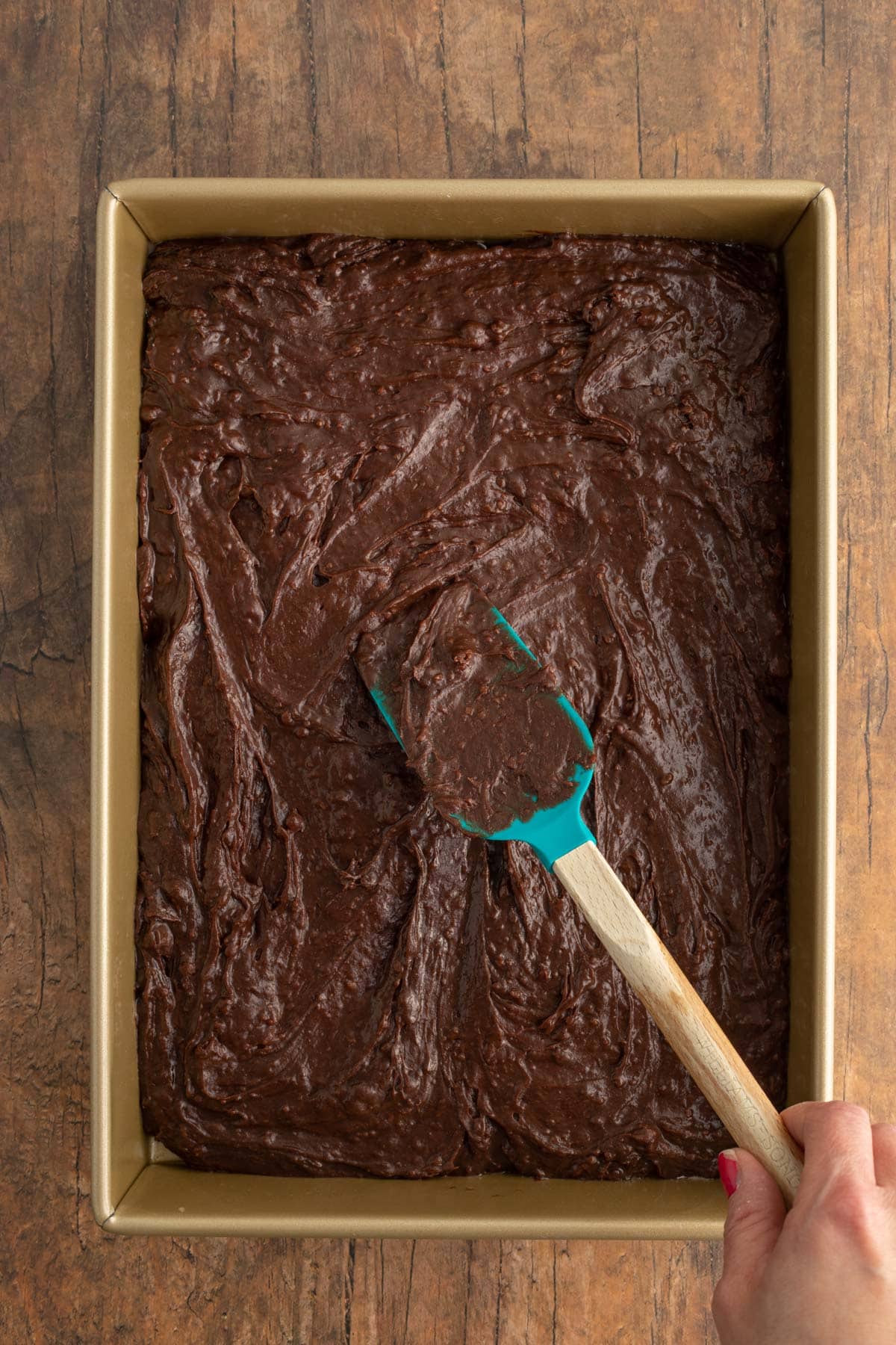 Cakey Brownies spreading batter in baking pan with spatula