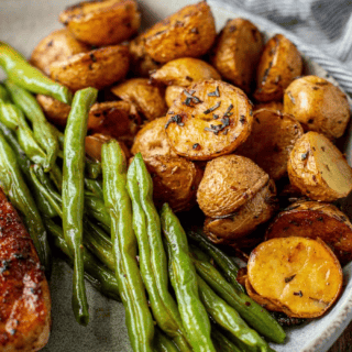 potatoes on a white plate being served with green beans and pork