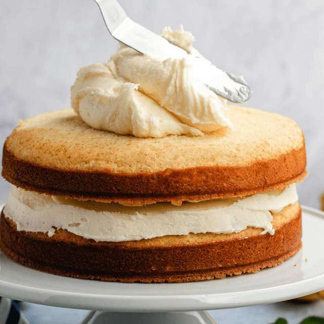spreading frosting on top of a two-layer cake on a white plater