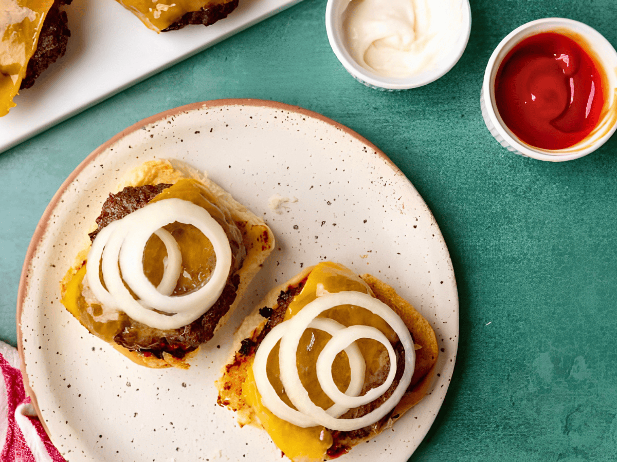 meat patties on bread buns with cheese and onions with a side of mayo and ketchup