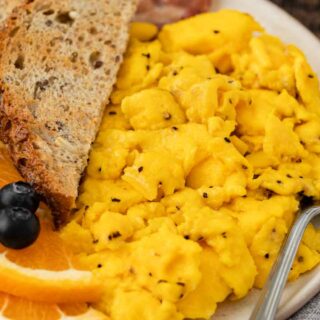 Close up of breakfast plate with toast, fruit, and scrambled eggs.