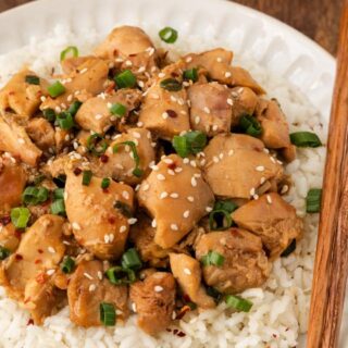 Chicken on a white plate with rice and chopssticks