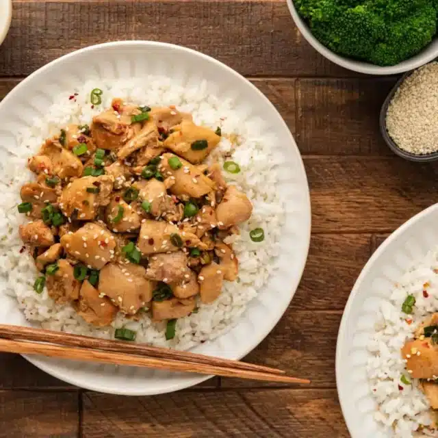 White plate with rice and chicken on top of a brown table