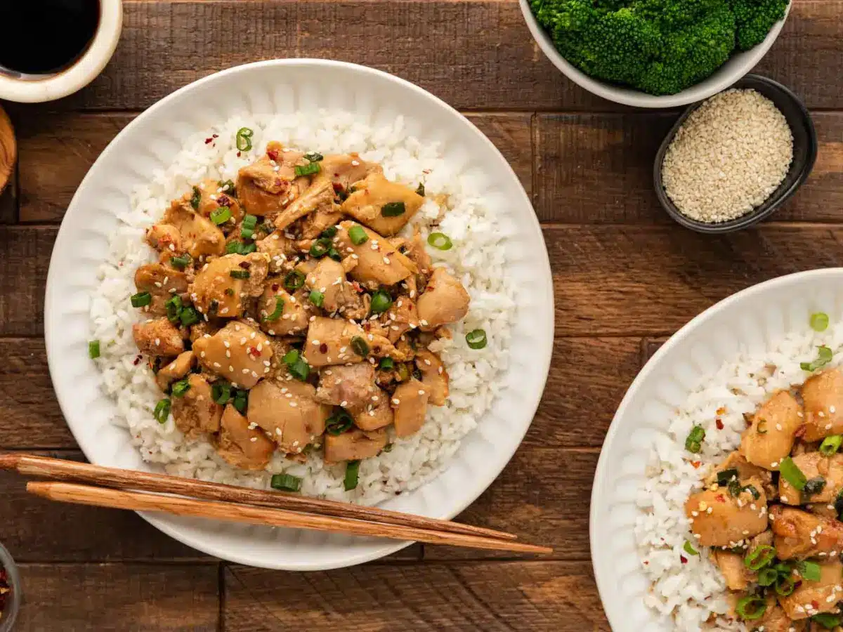 White plate with rice and chicken on top of a brown table
