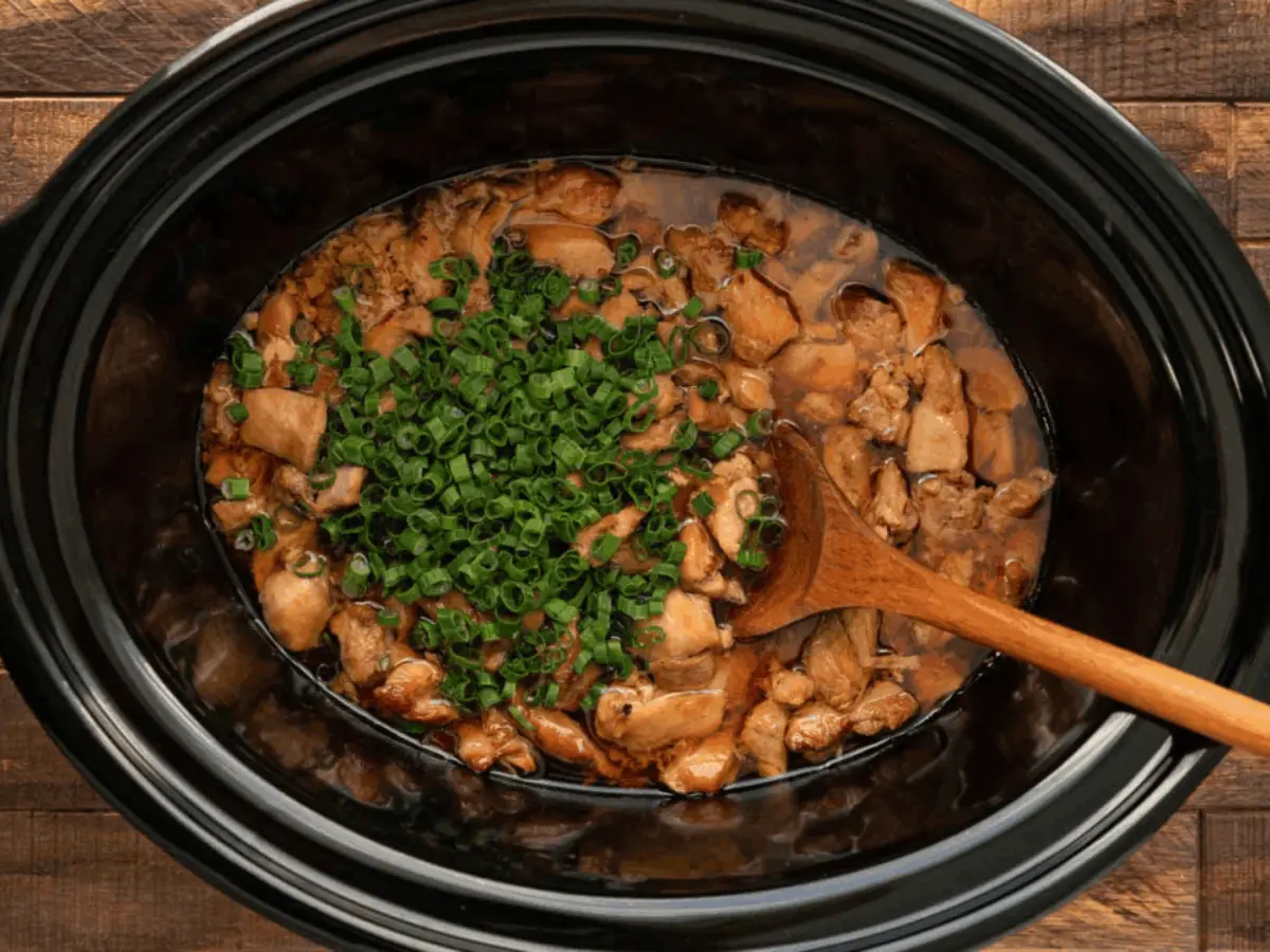Slow cooker with chicken in it with a brown spoon