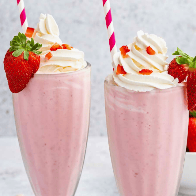 two cups of berry milkshakes topped with whipped cream and a straw on a table