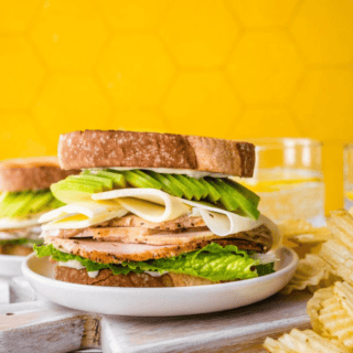 sandwich with apples and meat on a white plate with chips on the side