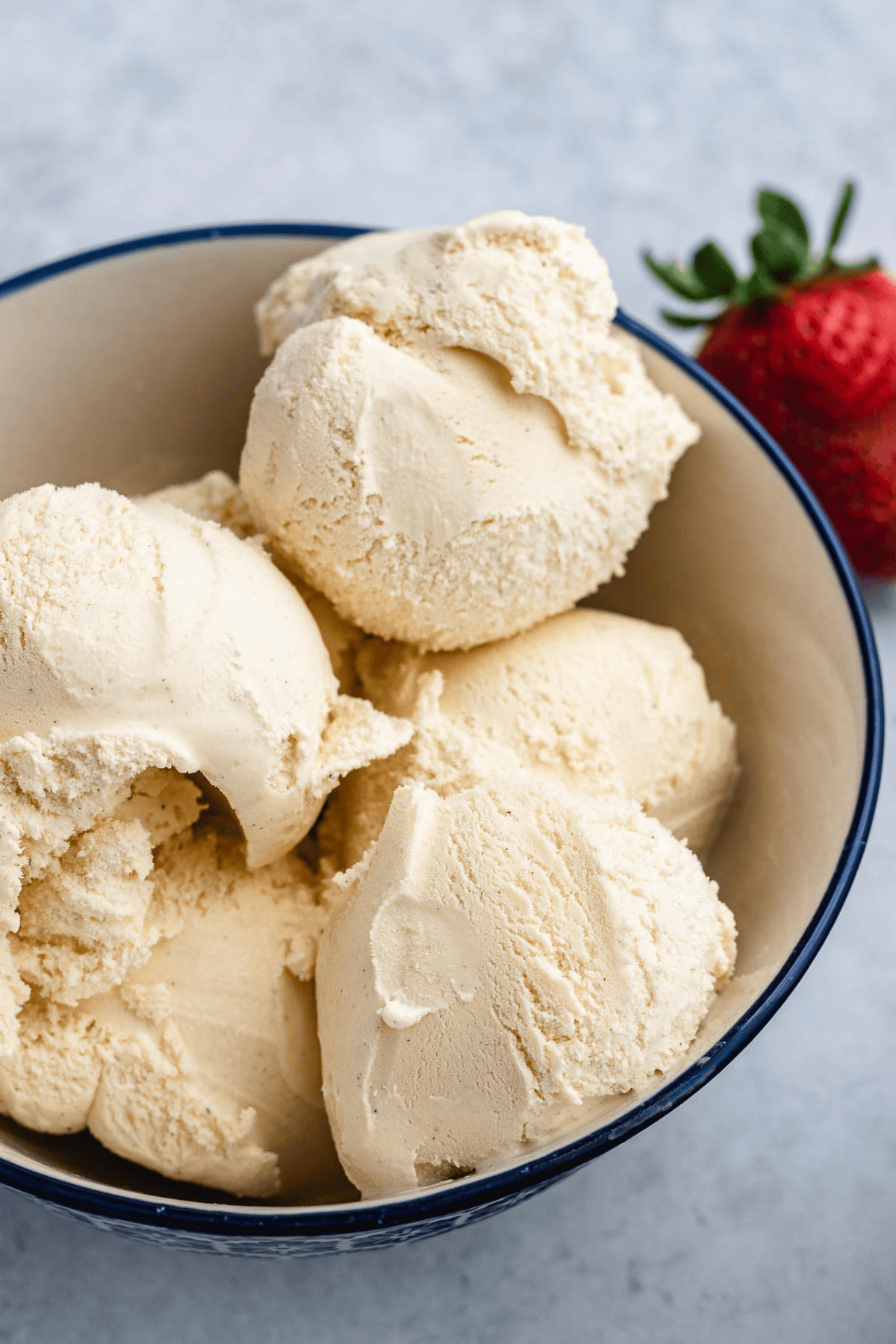 Vanilla ice cream scoops in a bowl with strawberries in the background