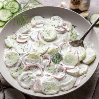 Sliced cucumbers, red onion, and creamy dressing on serving plate.