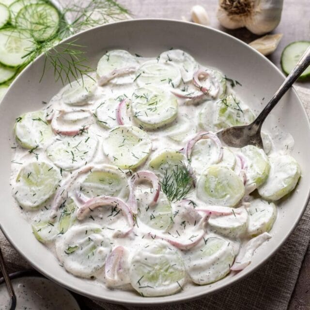 Sliced cucumbers, red onion, and creamy dressing on serving plate.
