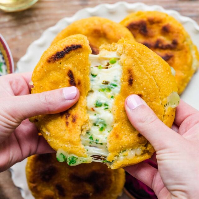 hands opening a pupusa to showcase the cheesy filling