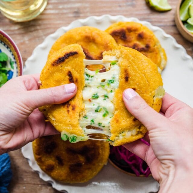 hands opening a pupusa to showcase the cheesy filling