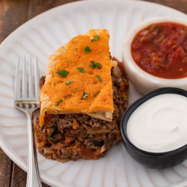 Cheesy Burrito Pie slice on a plate with salsa and sour cream