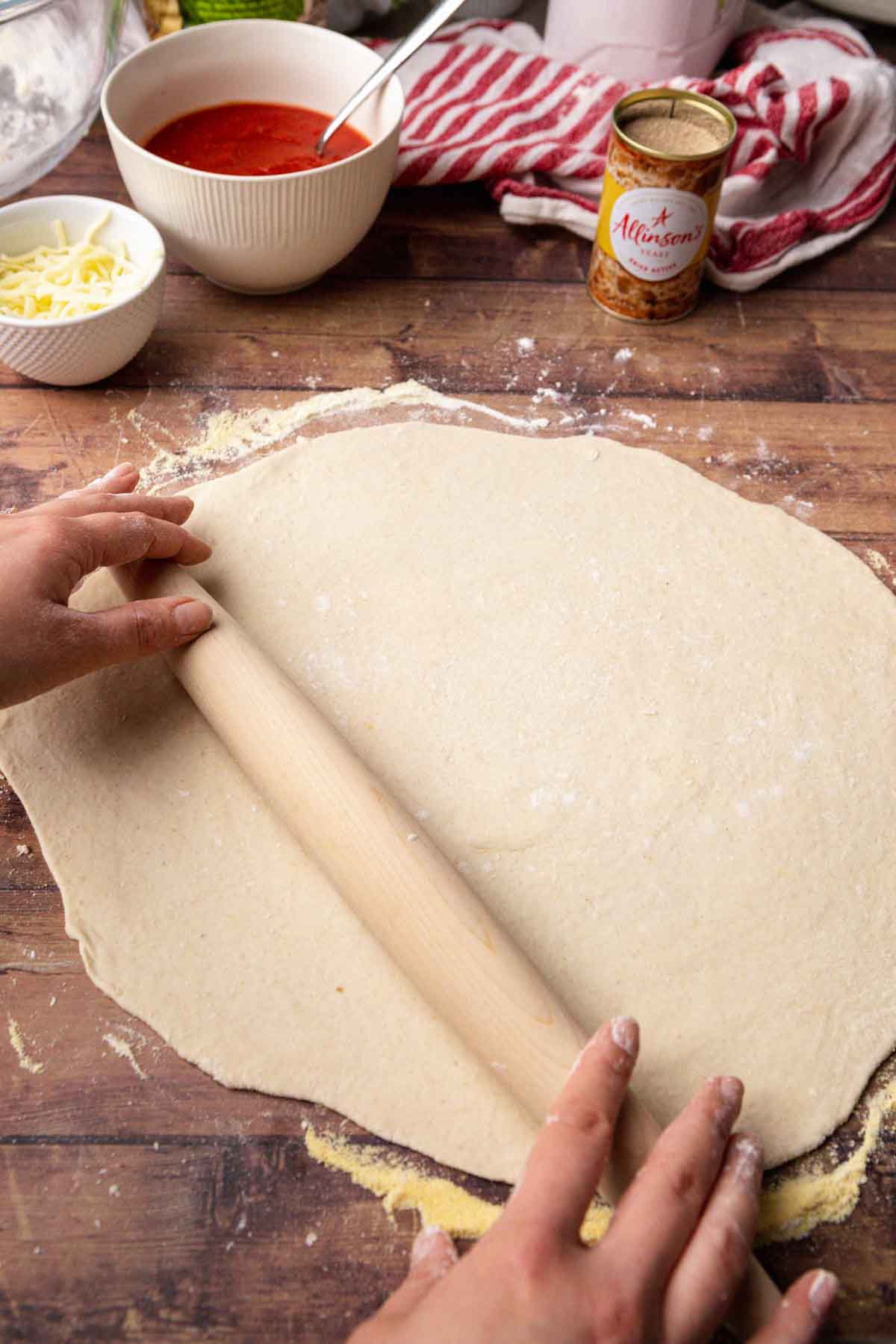 Thin Crust Pepperoni Pizza rolled out dough on wooden counter with rolling pin