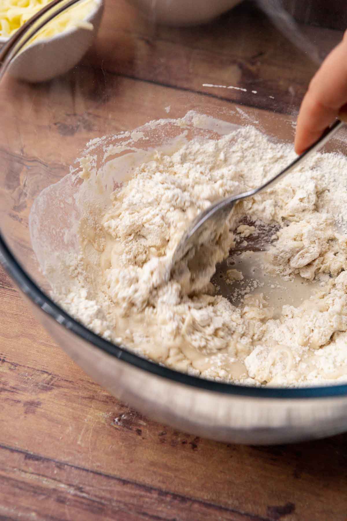 Thin Crust Pepperoni Pizza mixing flour into activated yeast mixture in bowl with spoon