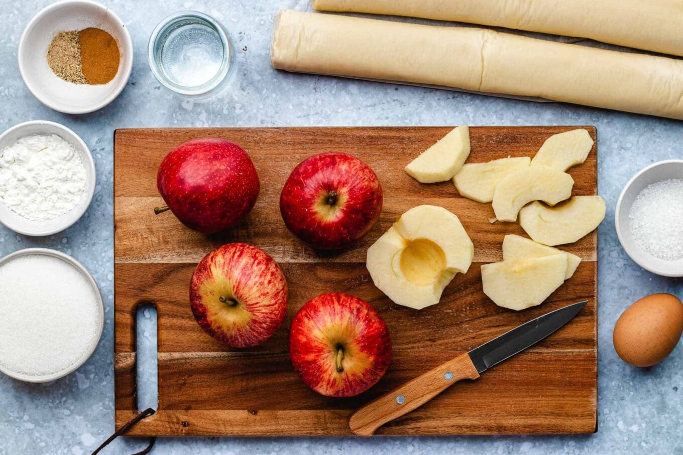 Apple Turnover ingredients spread out in prep bowls and apples on wooden board, some apples chopped, horizontal