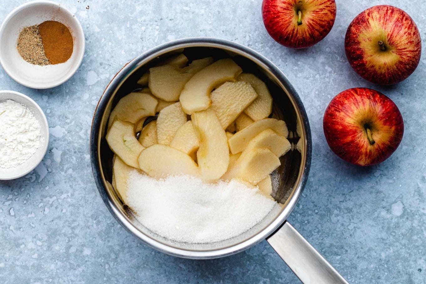 Apple Turnover apple slices and sugar in medium pan, whole apples and other ingredients in bowls around pan