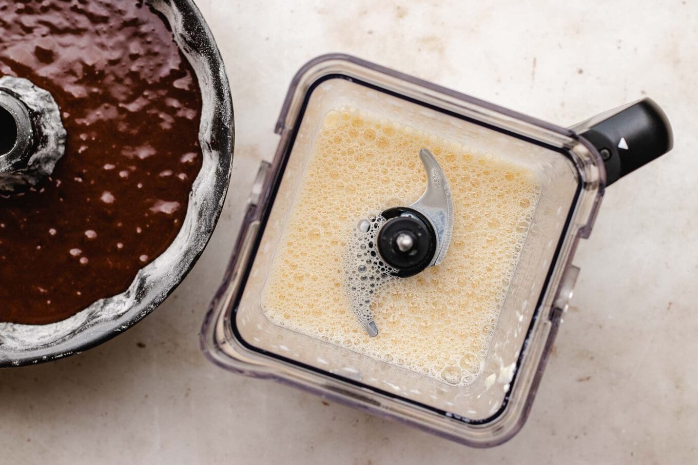 Chocoflan blender with blended flan batter next to Bundt pan with cake batter, horizontal photo