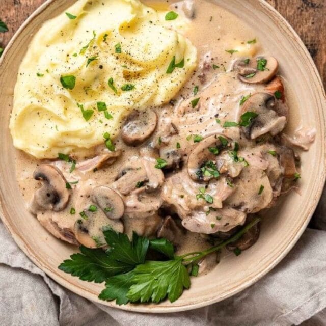 Sauce served over pork chops on a plate with mash potatoes.