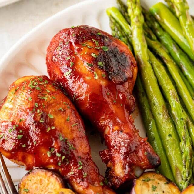 Two chicken drumsticks on dinner plate.