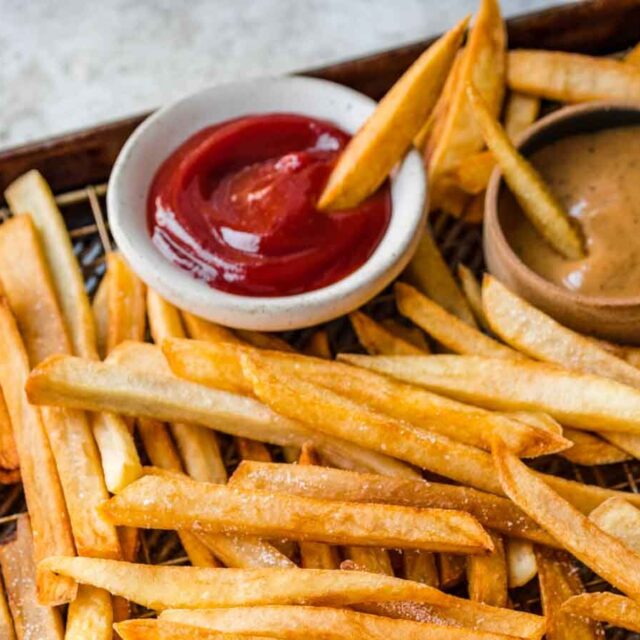 baking sheet of cooked french fries being dipped in sauce