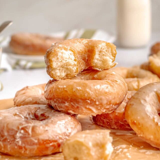 Glazed Potato Donuts finished donuts piled on parchment paper with top donut cut in half. 1x1 size