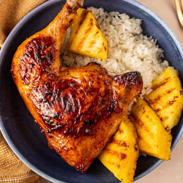 plated chicken leg quarters with pineapple wedges and white rice.