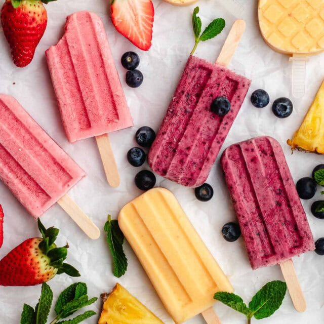 Homemade Popsicles frozen popsicles spread out on counter with fruit and berries in between popsicles, 1x1