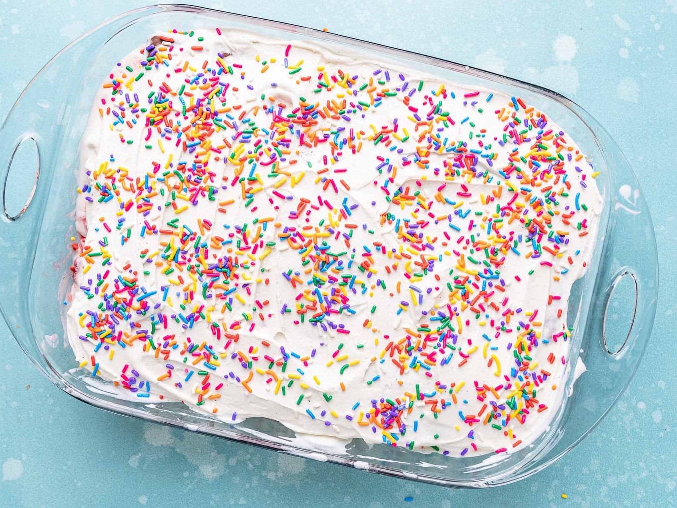 Ice Cream Sandwich Cake sprinkles added on top of ice cream cake in glass casserole dish.