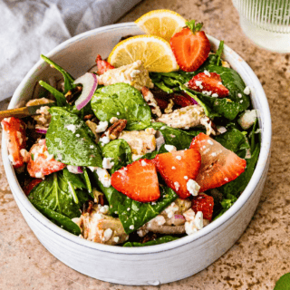 green veggies, berries, onions, chicken, and cheese salad in a white bowl