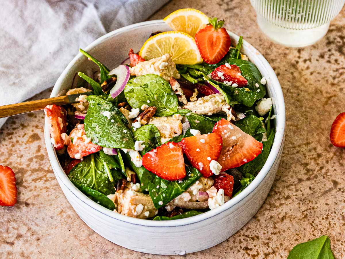 green veggies, verries, onions, chicken, and cheese salad in a white bowl
