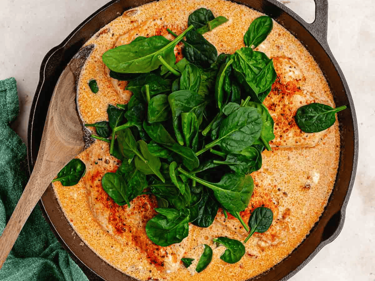 Spinach being added to cream sauce in pan.