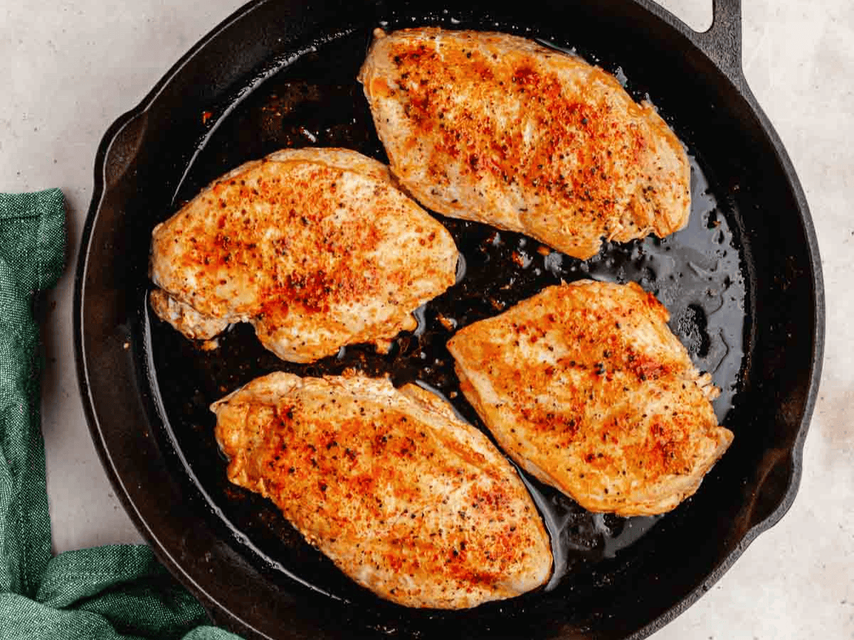Seasoned chicken breasts cooked in pan.