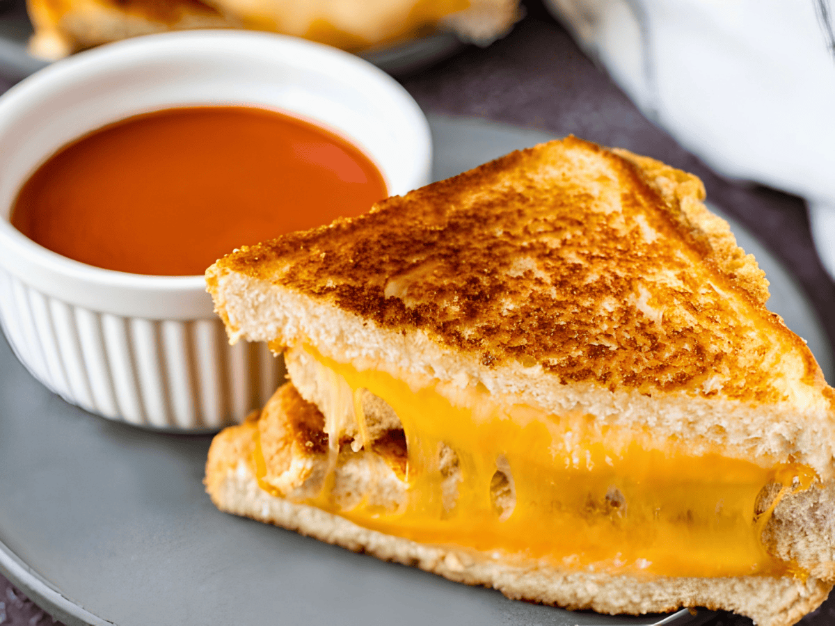 cheese pull in between slices of bread on a plate with tomato soup in white bowl