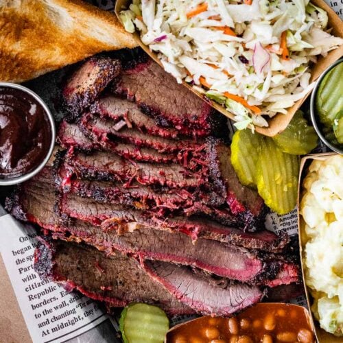 Ultimate Smoked Brisket sliced brisket plated on tray wit coleslaw, toast, pickle chips, BBQ sauce, and cauliflower.