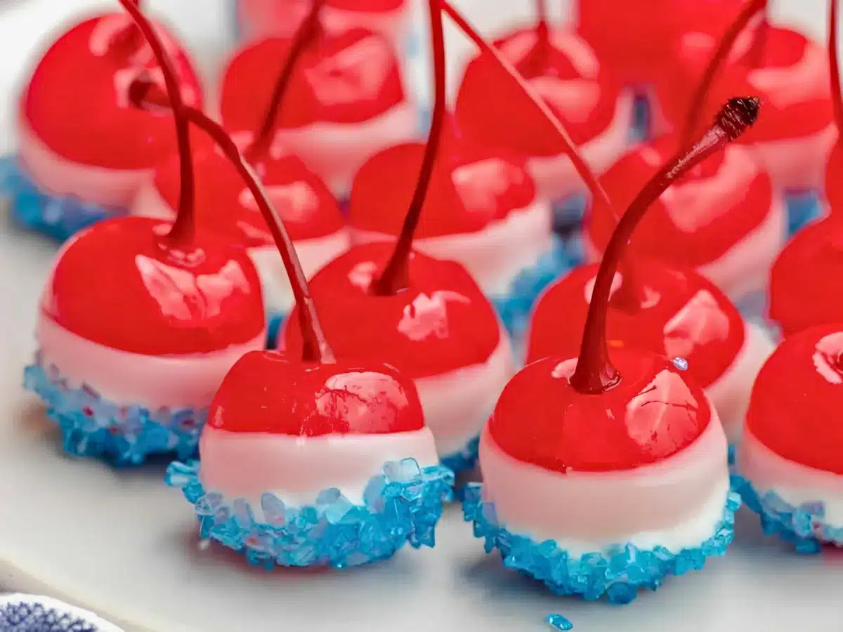 round red fruits with stems dipped in white chocolate and blue sugar side by side on a white plate