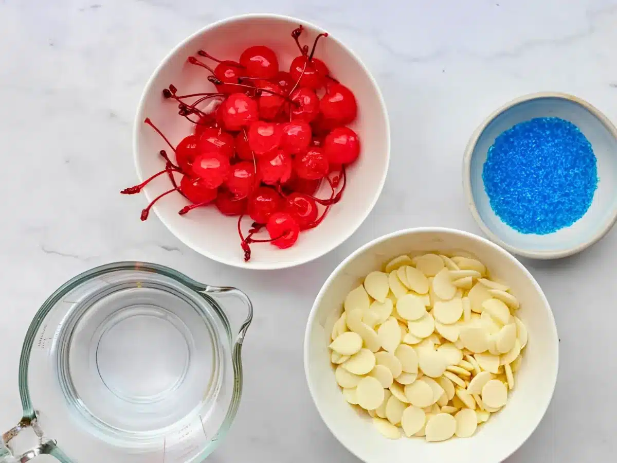 round red fruits, white chocolate, and blue sugar in white bowls with alcohol in measuring cup