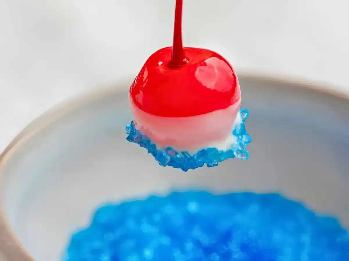 single red round fruit dipped in white chocolate and blue sugar above a bowl of blue sugar