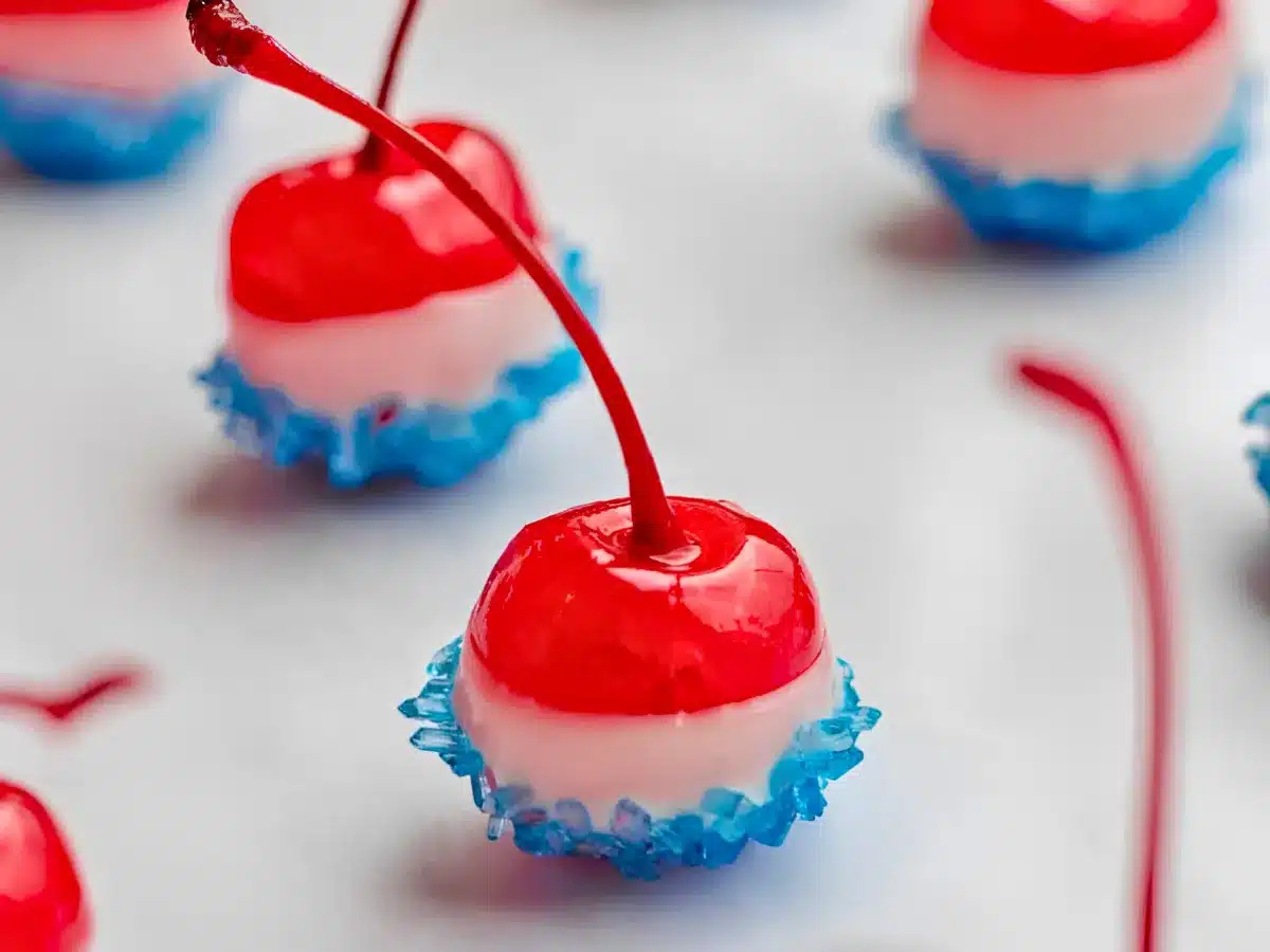 round red fruits with stems dipped in white chocolate and blue sugar spaced out on plate