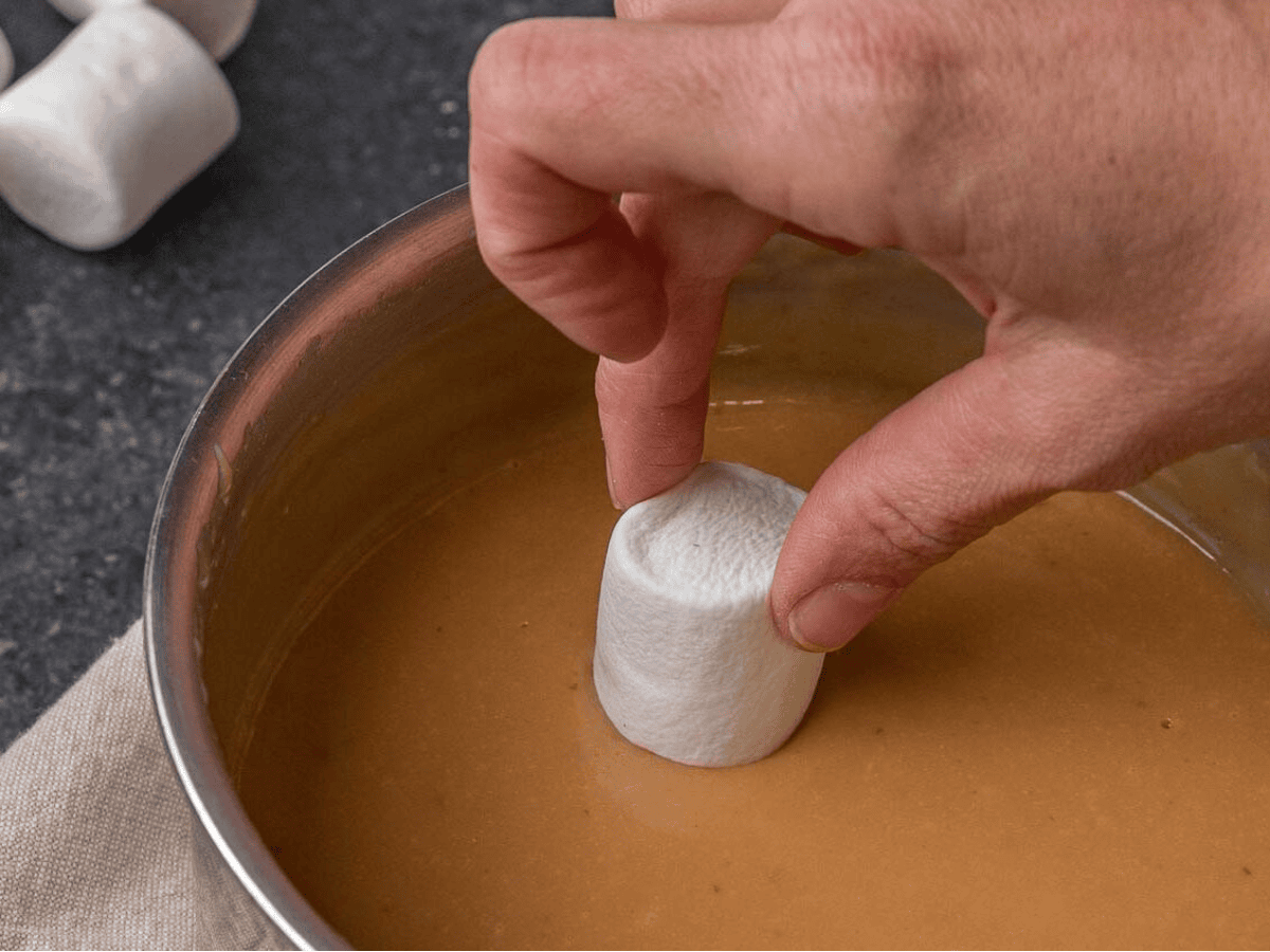 dipping a marshmallow into caramel