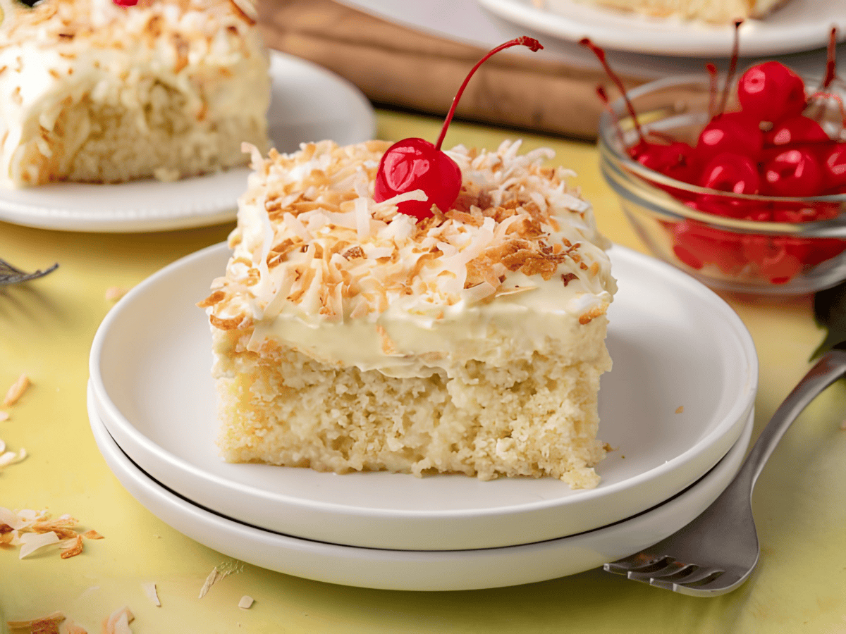 moist tropical cake with a cherry on top of a white plate with cherries in the back