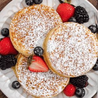 three pancakes dusted with powdered sugar. blackberries, strawberries and blueberries on the plate