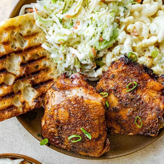 Plate with two cooked thighs, macaroni salad, slaw and bread
