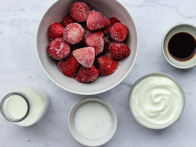 Frozen strawberries, sugar, milk, vanilla, and sugar in bowls