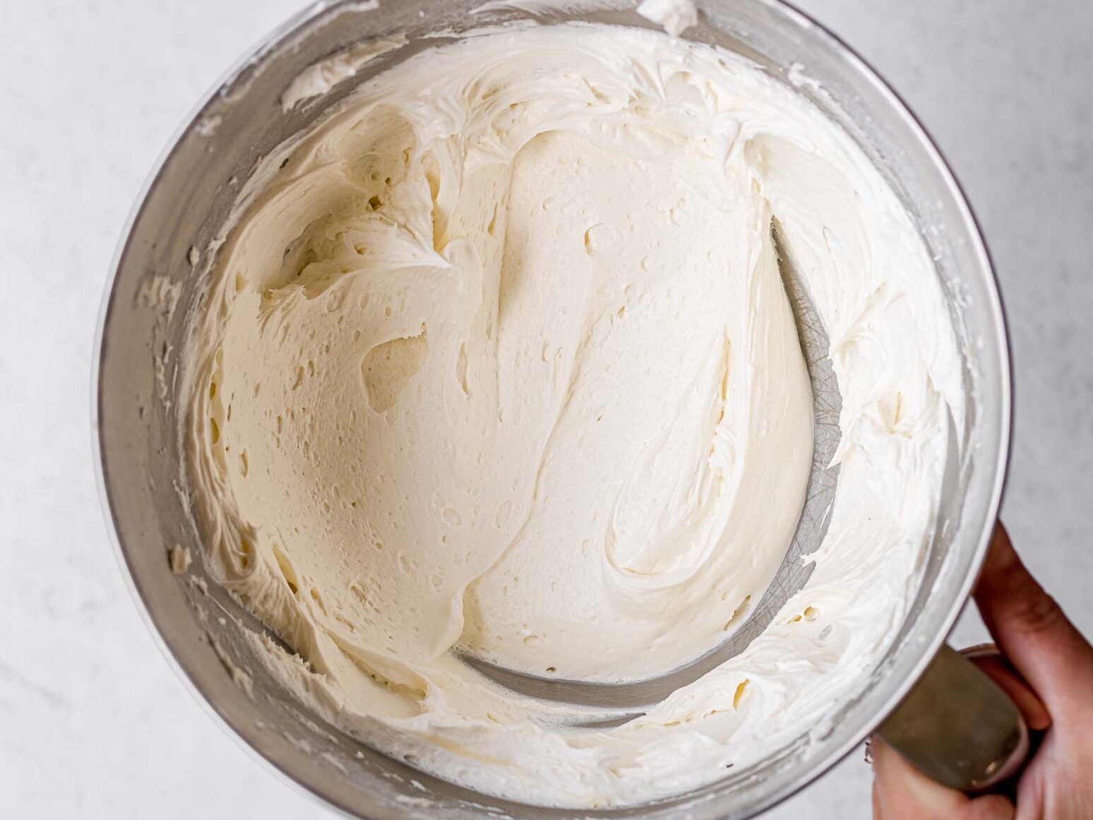 Unicorn Cupcakes frosting mixed in bowl and hand holding bowl handle.
